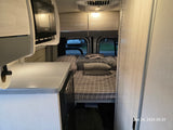 RV rental camper van interior featuring a bed, kitchenette with microwave, and sleek storage.
