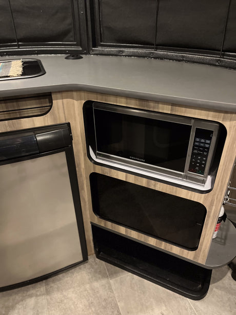 Compact kitchen area in an RV rental, featuring a built-in microwave, refrigerator, and sink. Perfect for on-the-go meals.