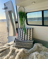 Cozy RV rental interior with black & white pillows & furry blanket, offering stunning ocean & beach views from the open back.