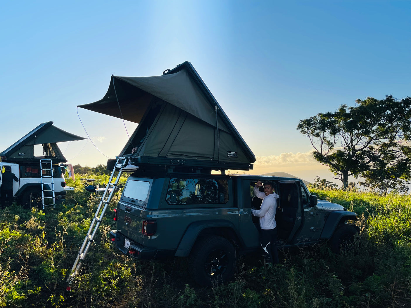 Adventure camping with an RV rental! Two Jeeps, equipped with rooftop tents, are set in a scenic outdoor landscape with a man.
