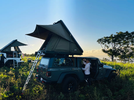 Adventure camping with an RV rental! Two Jeeps, equipped with rooftop tents, are set in a scenic outdoor landscape with a man.