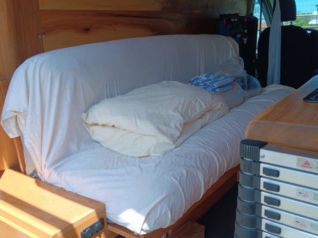 RV rental interior: custom wooden build with a comfortable bench/bed setup, white bedding, and travel essentials.