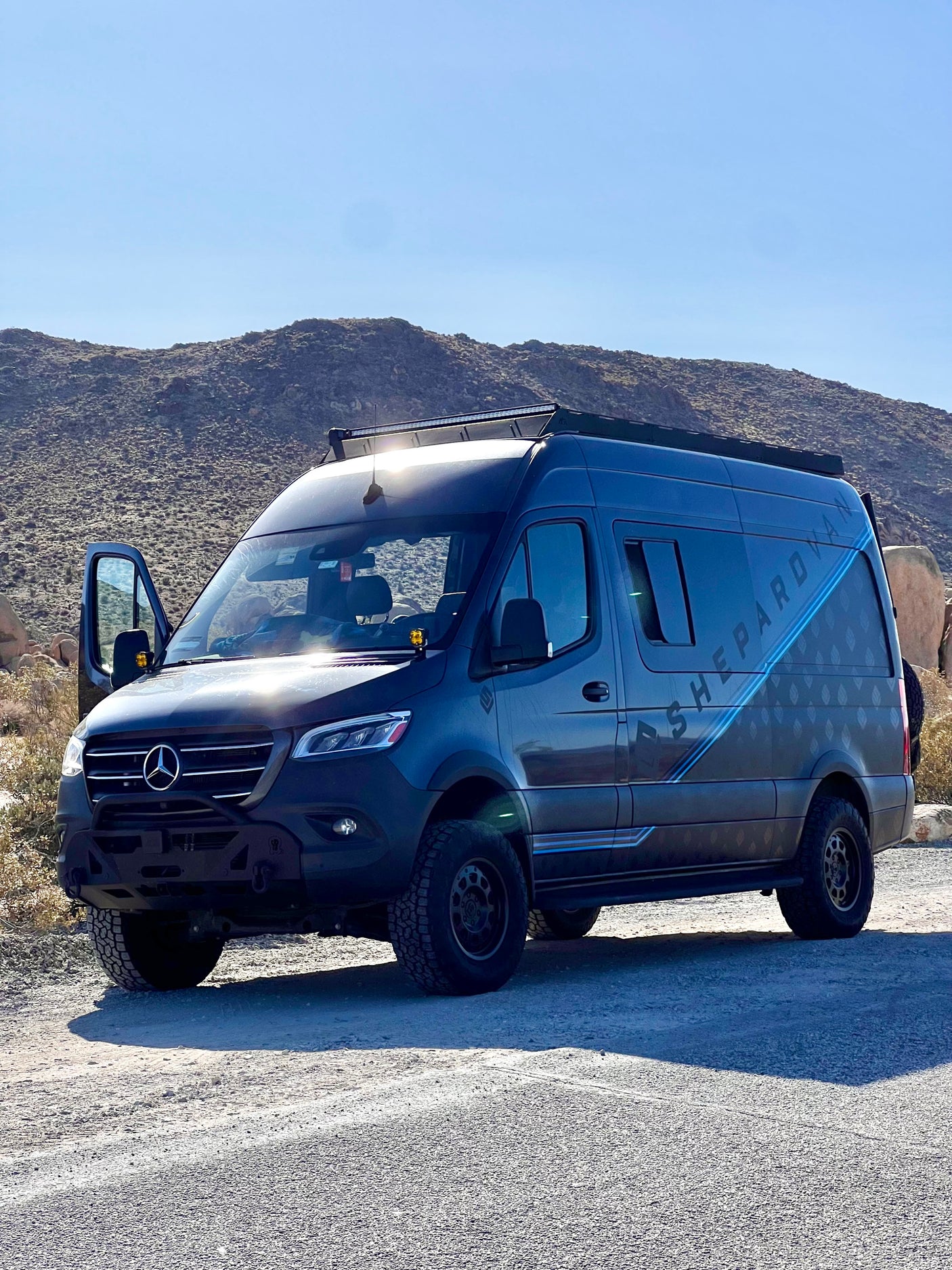 Adventure-ready gray Mercedes-Benz Sprinter van, an off-road RV rental parked in a sunny, desert landscape.