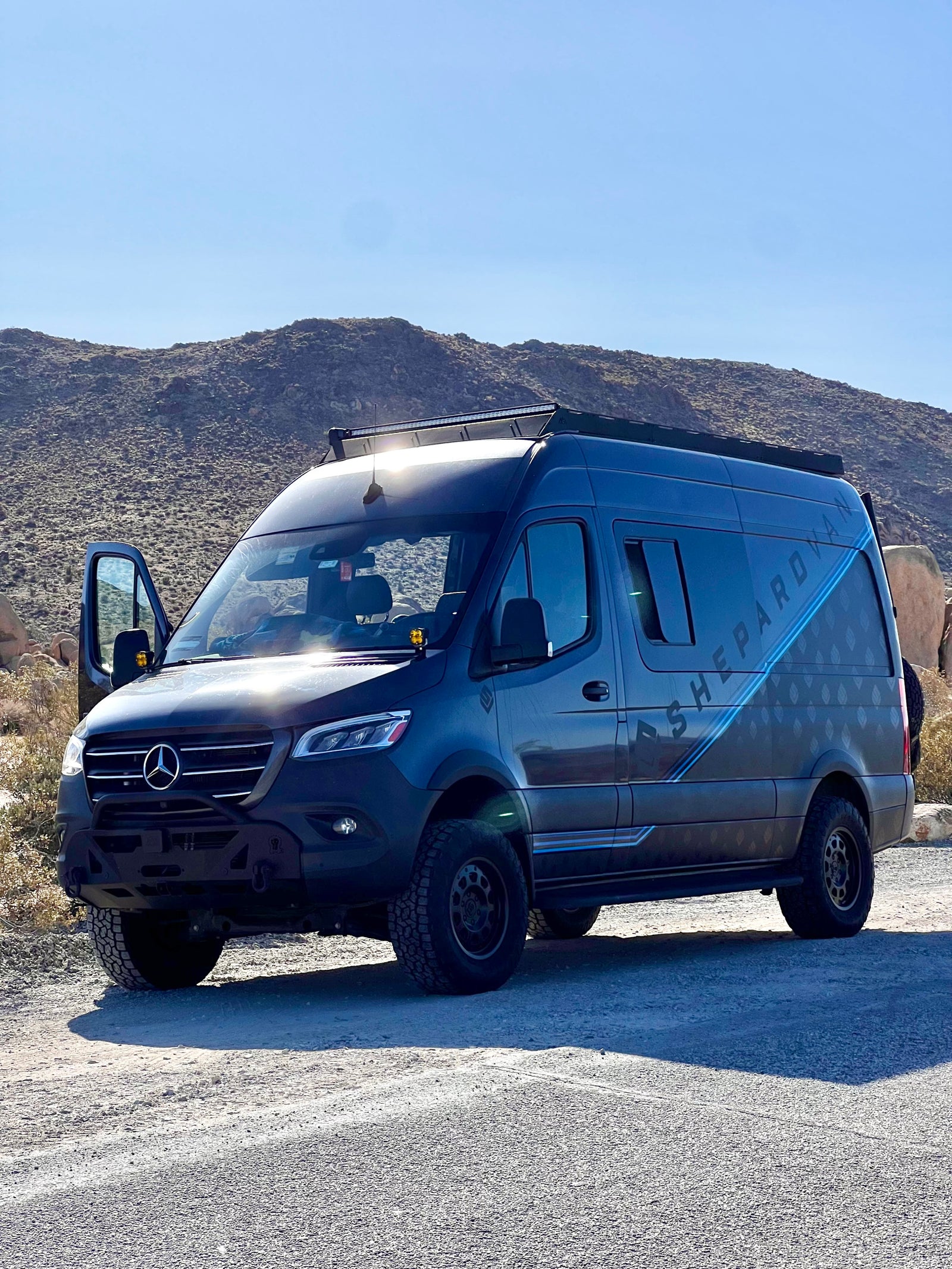 Adventure-ready gray Mercedes-Benz Sprinter van, an off-road RV rental parked in a sunny, desert landscape.
