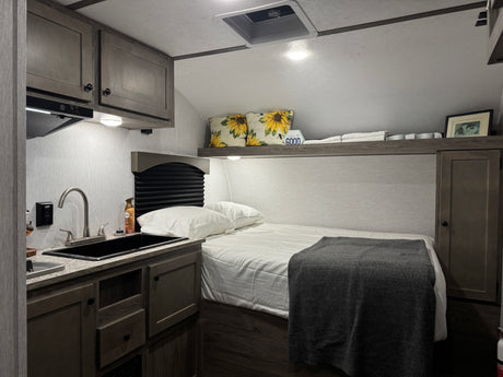 RV rental: a cozy interior featuring a bed with a grey blanket, next to a functional kitchenette with a black sink.