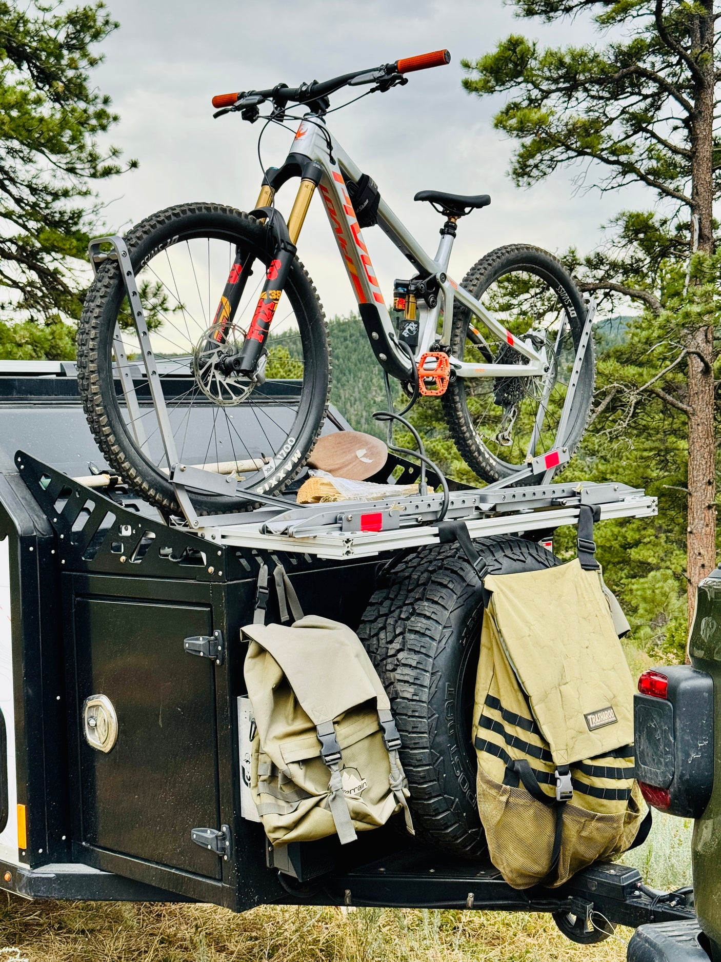 Mountain bike secured on an RV rental trailer's roof rack, with spare tires and bags packed for an outdoor adventure.
