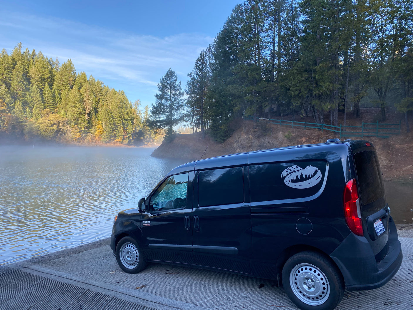 A dark blue Ram ProMaster City camper van on a misty lake boat ramp, perfect for your next RV rental adventure.