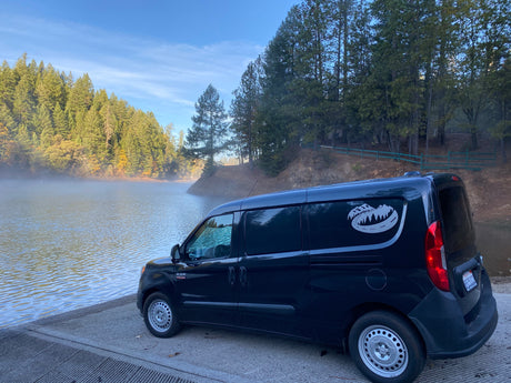 A dark blue Ram ProMaster City camper van on a misty lake boat ramp, perfect for your next RV rental adventure.