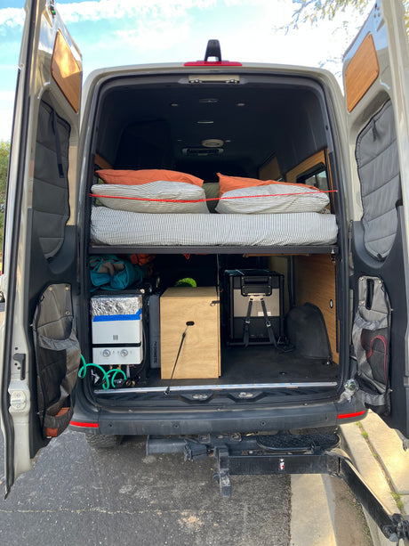 RV rental with custom camper van conversion, featuring a raised bed, Dometic fridge, and portable shower for adventure.