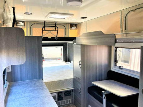Inside an RV rental: a compact living space featuring a bed, dinette with table, and counter area.