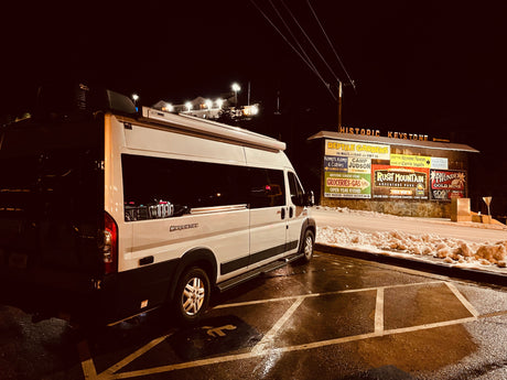 A white RV rental is parked at night in a snowy lot at Historic Keystone, with an illuminated sign for attractions.