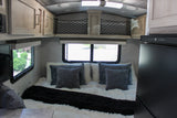 Cozy RV rental bedroom featuring a plush bed with white and gray pillows, overhead storage, and windows with outdoor views.