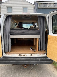 Back view of an **RV rental**: a converted camper van interior with a bed, storage, and wood paneling, ready for adventure travel.
