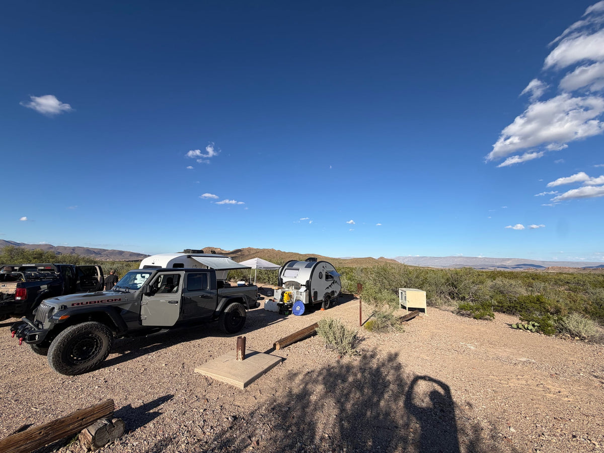  parked on asphalt in a grassy field under cloudy skies.|A nüCamp teardrop RV rental with red underglow hitched to a dark car — photo 5