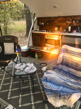 Cozy rv rental camping: outdoor kitchen, dinner for two, and warm blankets under a glowing sunset.