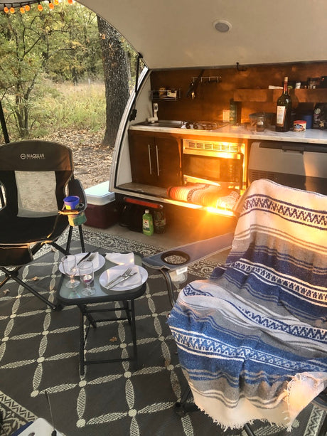Cozy rv rental camping: outdoor kitchen, dinner for two, and warm blankets under a glowing sunset.