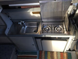 Inside this RV rental: a compact kitchen with stainless steel sink, two-burner stove, and small fridge.