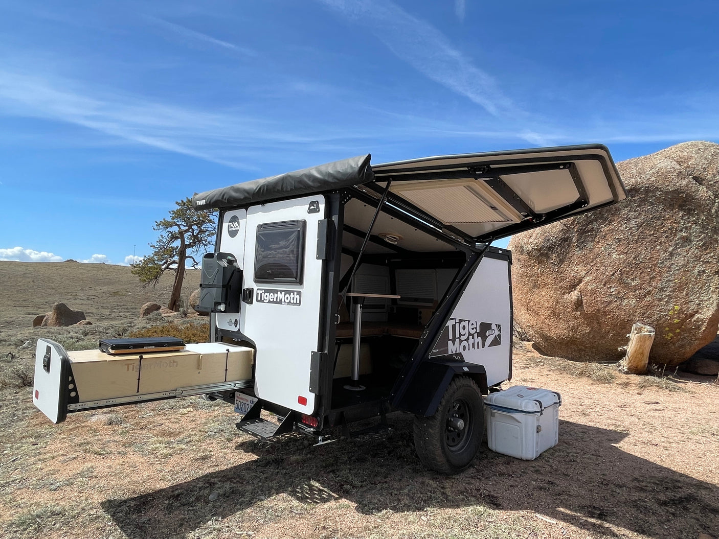 Compact Taxa TigerMoth trailer, ideal for RV rental, set up for remote camping amidst rocks and open land.