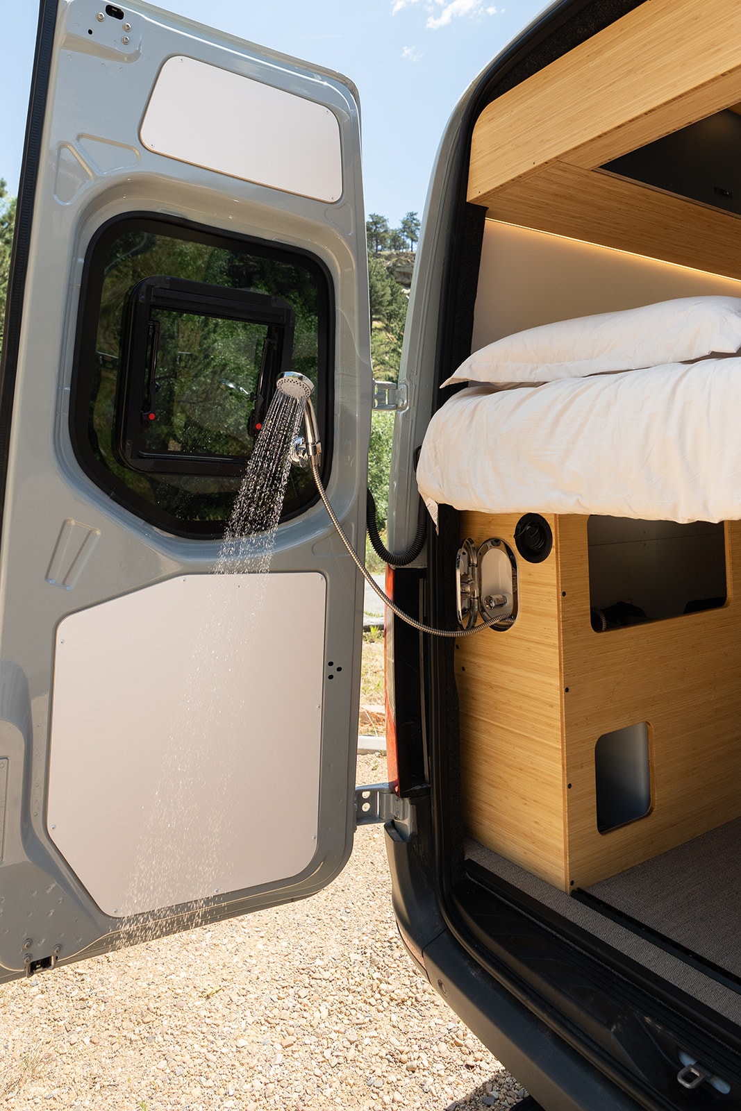 This RV rental features an outdoor shower setup from its open rear door, with a comfortable bed visible inside. — photo 20