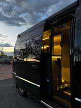 Inside this sleek black rv rental: warm lights, a screen door, fire extinguisher, and pet bowls. Perfect for cozy evenings on the road.