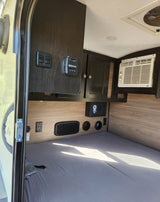 RV rental interior view: compact sleeping area with an AC unit, thermostat, and storage cabinetry clearly visible.