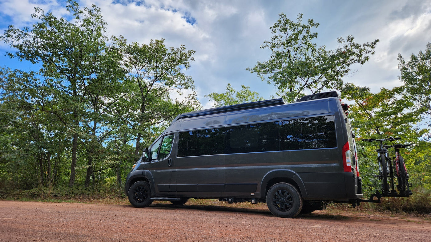 Dark grey RV rental with bikes on back, parked on dirt road in green forest. Perfect for nature adventures. — photo 8