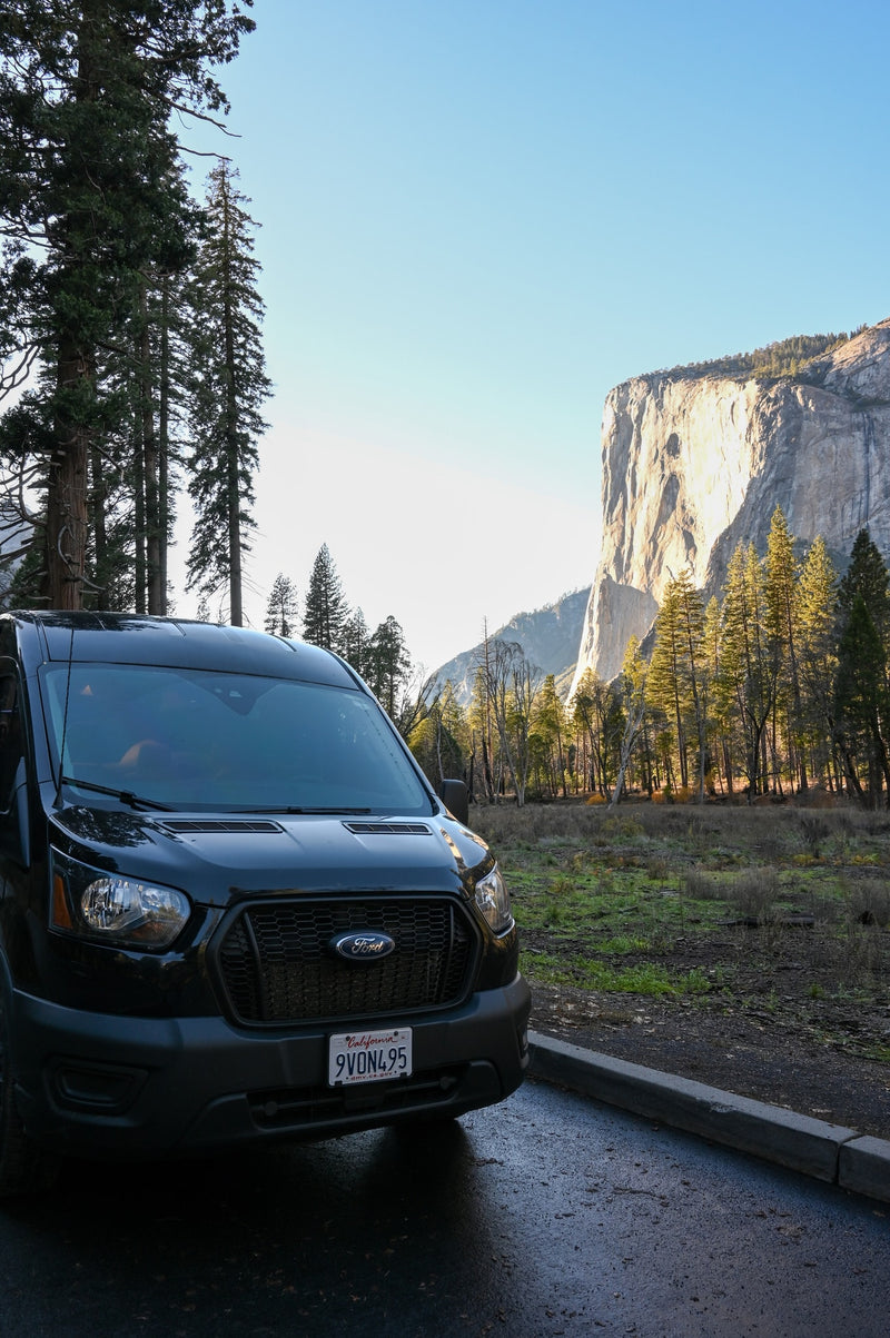 Black RV rental van parked in a scenic valley with towering trees and a massive sunlit cliff in the background. — photo 14