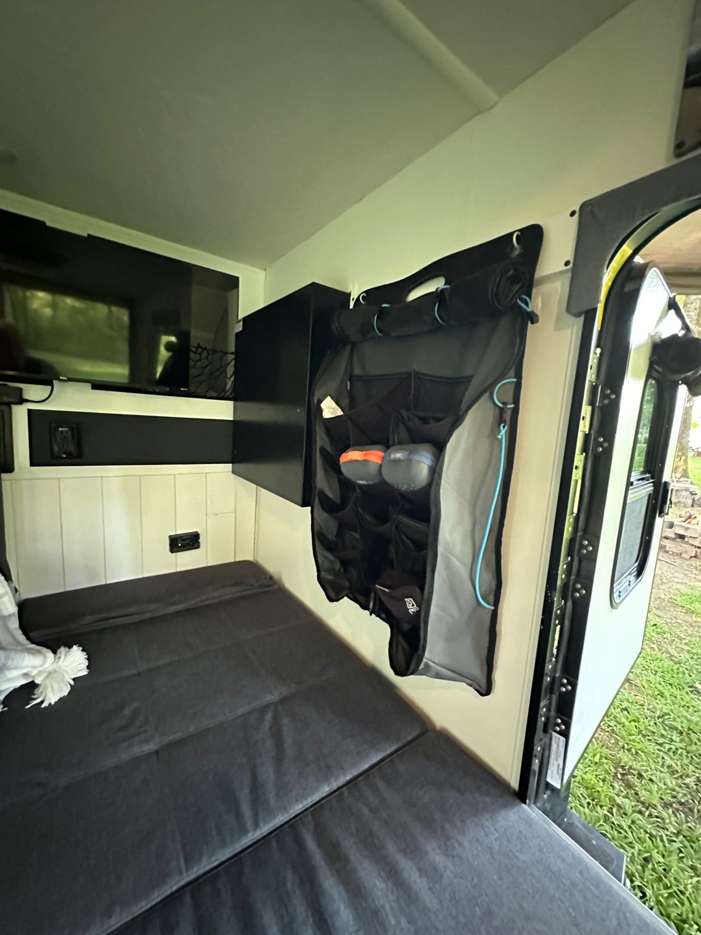 RV rental interior features a compact bed, wall-mounted TV, and a convenient hanging storage organizer near the open door. — photo 9
