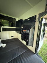 RV rental interior features a compact bed, wall-mounted TV, and a convenient hanging storage organizer near the open door.
