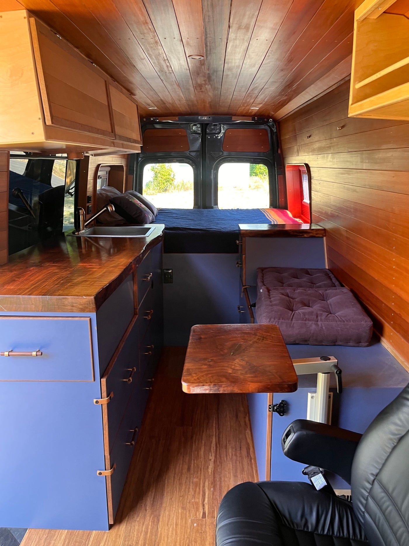Cozy custom RV rental interior with warm wood finishes, blue accents, and a versatile bed/workspace setup. — photo 13