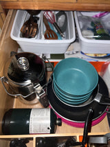 RV rental kitchen drawer stocked with cooking gear: propane, pots, pans, bowls, & utensils for camping trips.