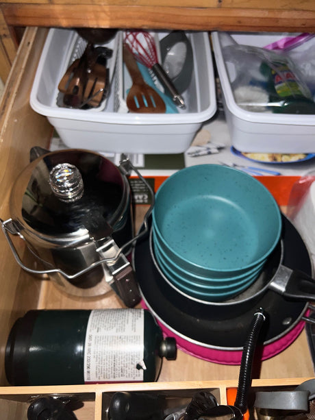 RV rental kitchen drawer stocked with cooking gear: propane, pots, pans, bowls, & utensils for camping trips.