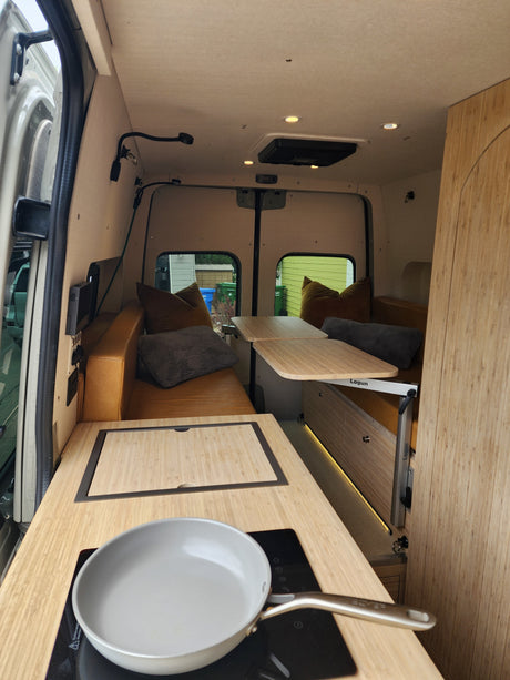 Inside a modern rv rental: a light-filled camper van with a compact kitchen, adaptable dining tables, and plush bench seating.