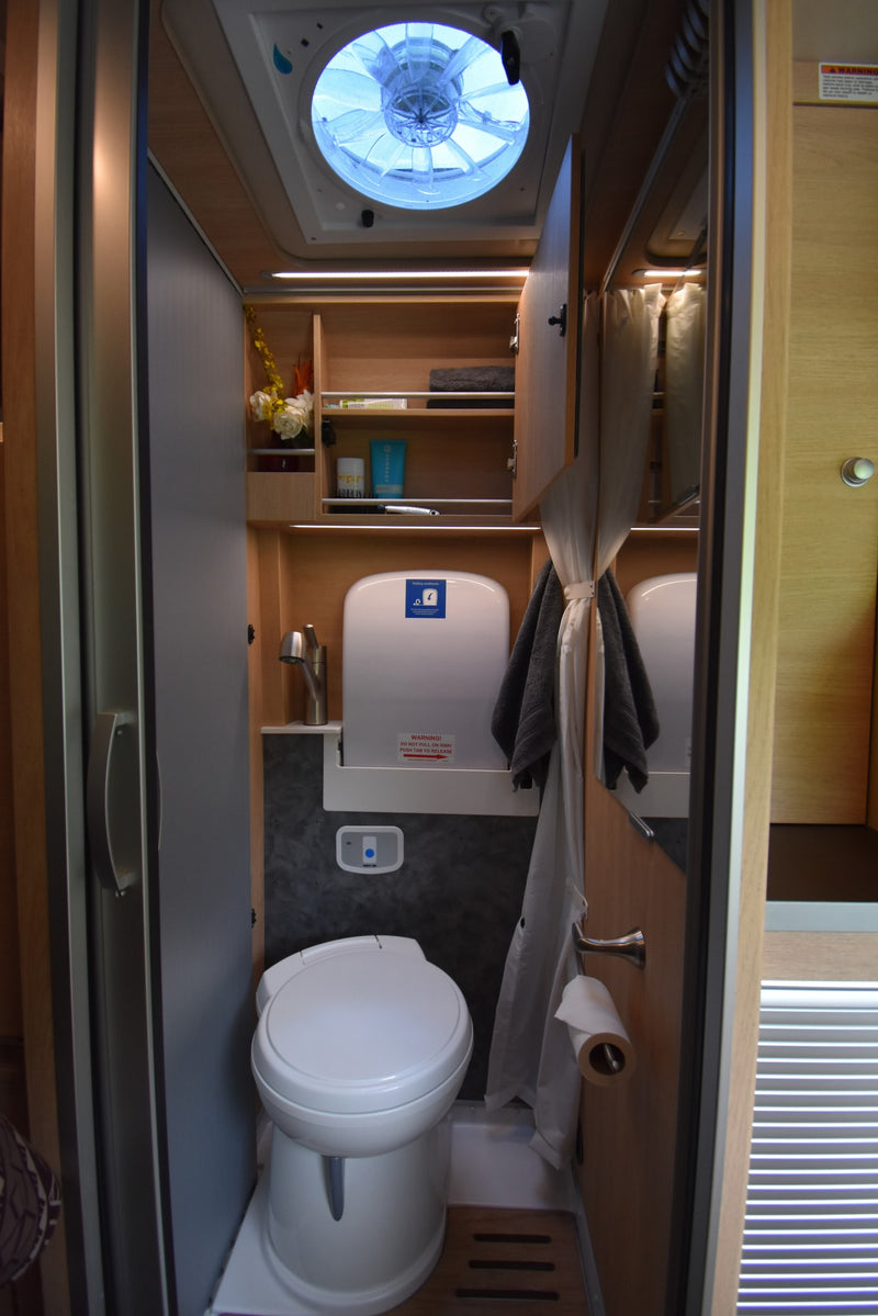 This RV rental's compact wet bath features a toilet, folding sink, shower curtain, overhead fan, and integrated storage. — photo 7
