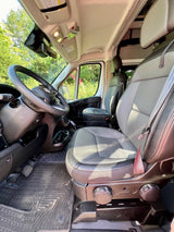 Front interior of an RV rental van, featuring two-tone seats, steering wheel, and clean floor mats. Ready for travel.