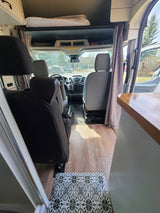 Comfortable RV rental interior: view from rear, showcasing custom curtains, wood flooring, and the driver's cab. Ideal for road trips.