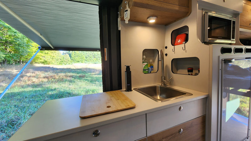 This RV rental offers a compact kitchen with a sink, microwave, and an outdoor view under an extended awning. — photo 15