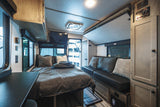 RV rental interior showcasing a comfortable bed, lounge sofa, control panels, and storage. Ideal for travel.