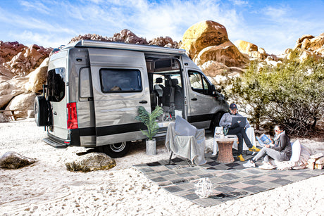 Relax and work remotely in nature with an **rv rental**! Two people enjoy a modern camper van setup in a desert landscape.