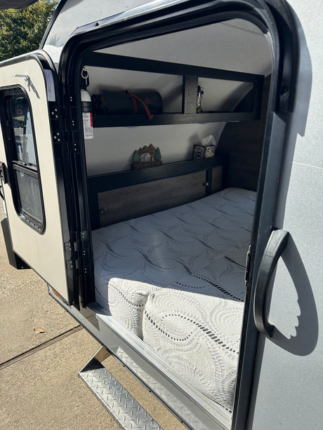 Inside a cozy rv rental: patterned mattress, dark wood headboard with cubbies, and shelves for camping essentials.