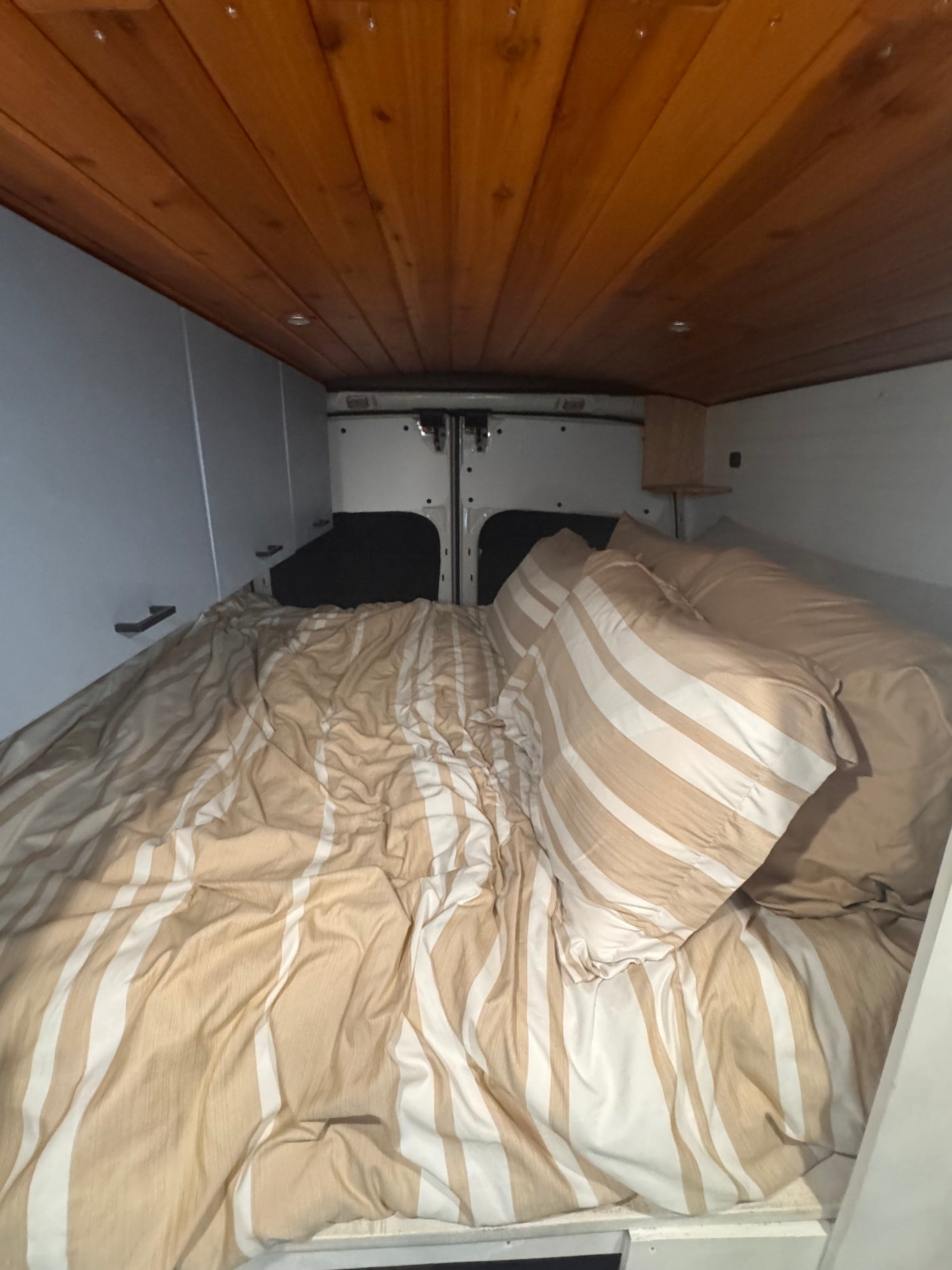 Interior of an RV rental: a cozy bed with striped bedding, wood ceiling, and storage cabinets.