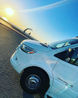 White RV rental at a scenic ocean view basketball court during sunset, with a person playing in the background.