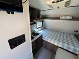 Inside this cozy rv rental: compact kitchen with sink, comfy bed with plaid bedding, mounted TV, and control panel for an easy trip.