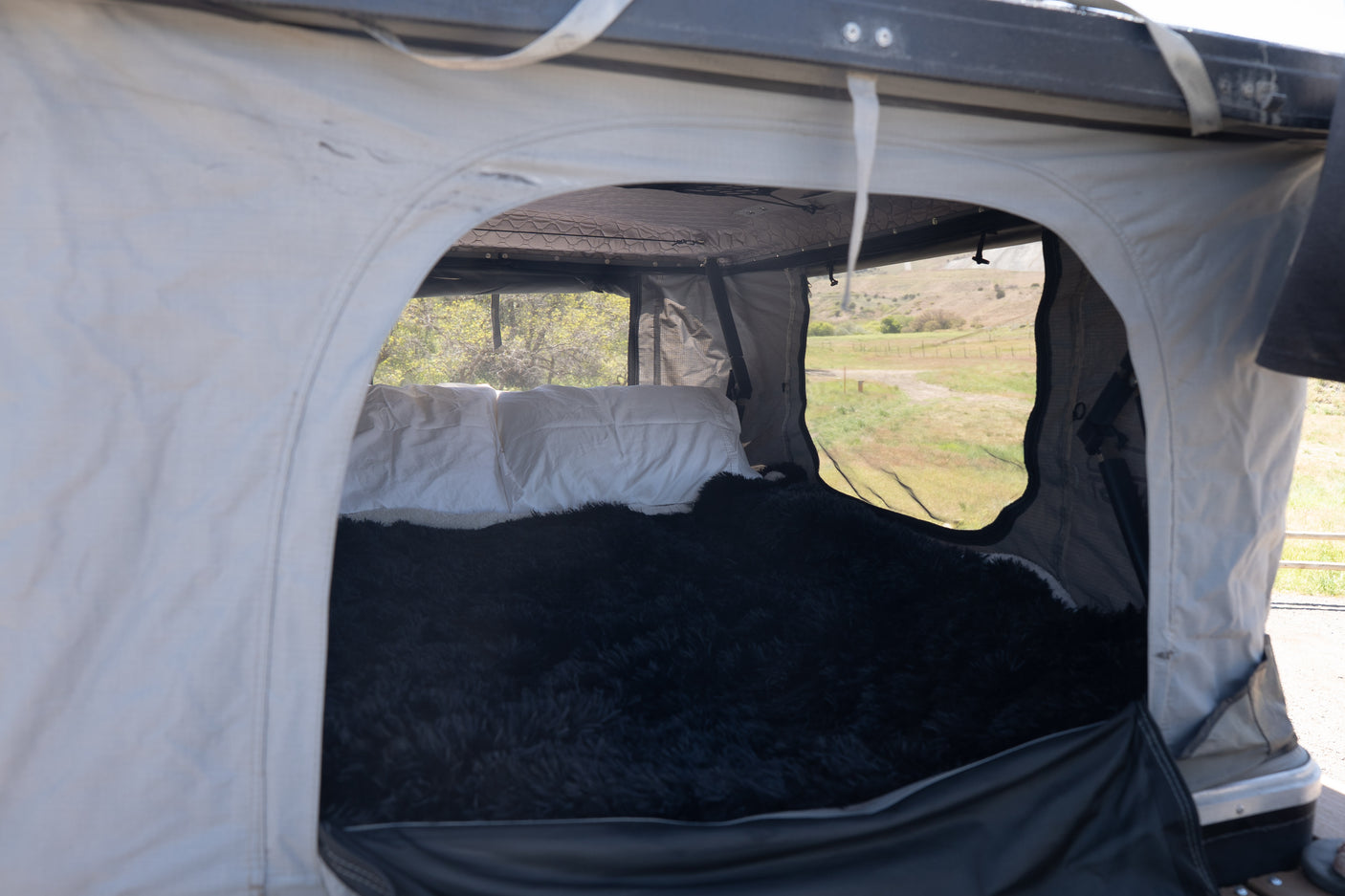 Cozy interior of an RV rental rooftop tent with a comfy bed, pillows, and scenic outdoor views through mesh windows.