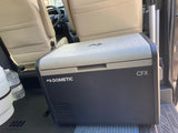A Dometic CFX portable cooler rests inside an RV rental, positioned near passenger seats for travel.