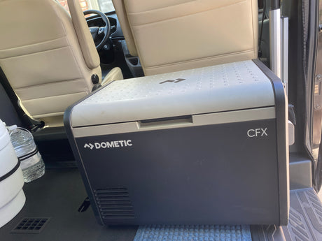A Dometic CFX portable cooler rests inside an RV rental, positioned near passenger seats for travel.