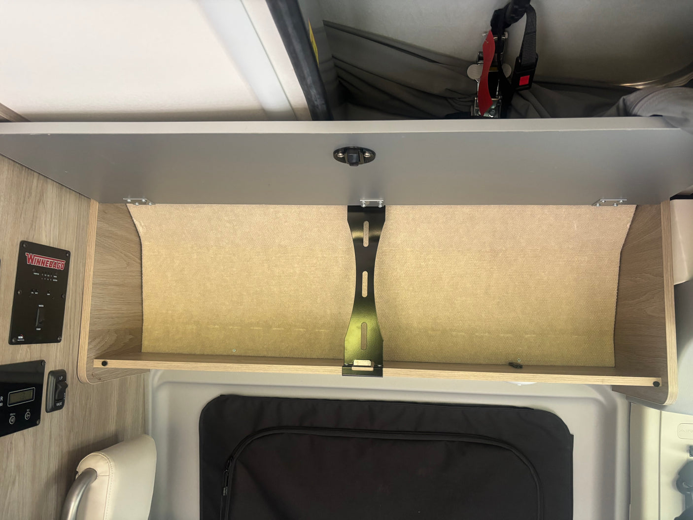 Open overhead storage in an RV rental, featuring a Winnebago control panel and hinting at a pop-top sleeping area above.