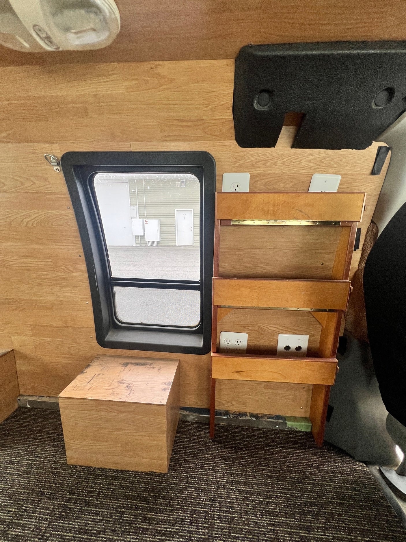 RV rental interior with wood paneling, carpeted floor, window, and custom shelf unit featuring power outlets.
