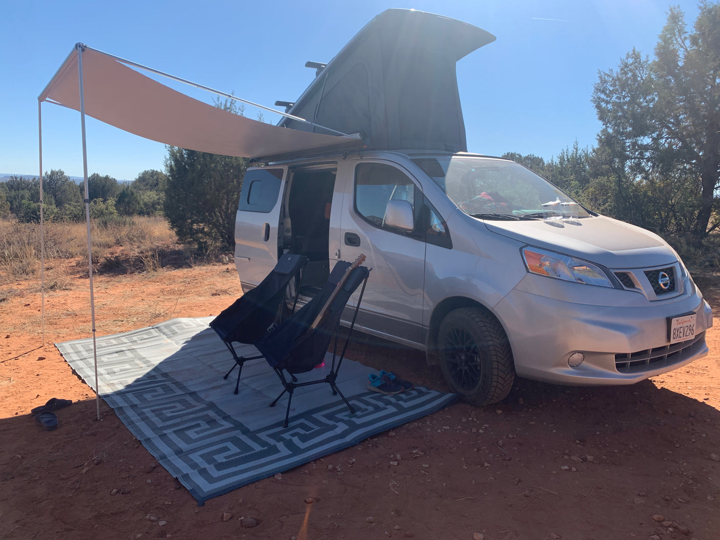 Pop-top camper van with awning & chairs set up on red dirt for a sunny outdoor adventure. Perfect rv rental.