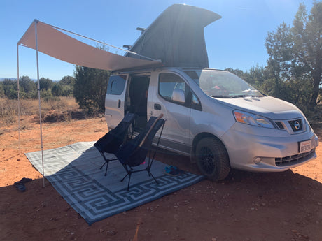 Pop-top camper van with awning & chairs set up on red dirt for a sunny outdoor adventure. Perfect rv rental.